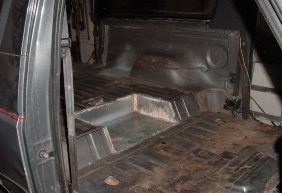 Stripped interior cargo floor of a gray SUV showing bare rusty metal floor pan with seats and carpet removed