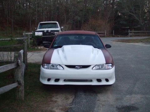 1995 Ford Mustang - A red and white 1995 Ford Mustang is parked in front of a white truck.
