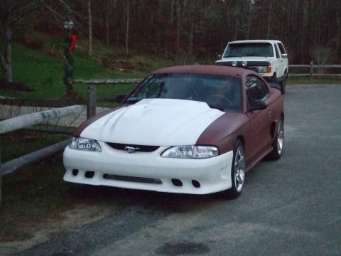 1995 Ford Mustang - A modified Ford Mustang is parked outside with a white SUV in the background.