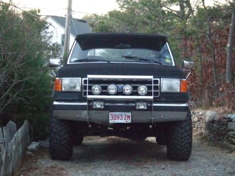 1995 Ford Mustang - This black SUV is parked outdoors, with a wooden fence to the left and trees to the right.