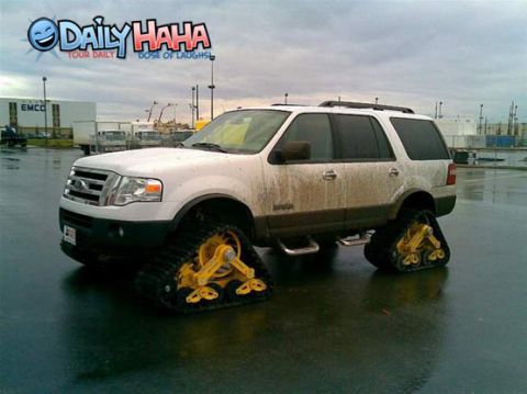 1998 Ford Crown Victoria - White Ford Expedition full-size SUV converted to run on four yellow-framed rubber track units in place of wheels, splattered with mud and p…