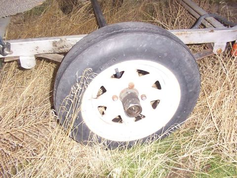 2003 Ford Ranger - Close-up of a trailer wheel, showing the tire and rim against a backdrop of dry grass.