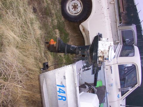 2003 Ford Ranger - A boat with an outboard motor is parked on a trailer next to a white truck.