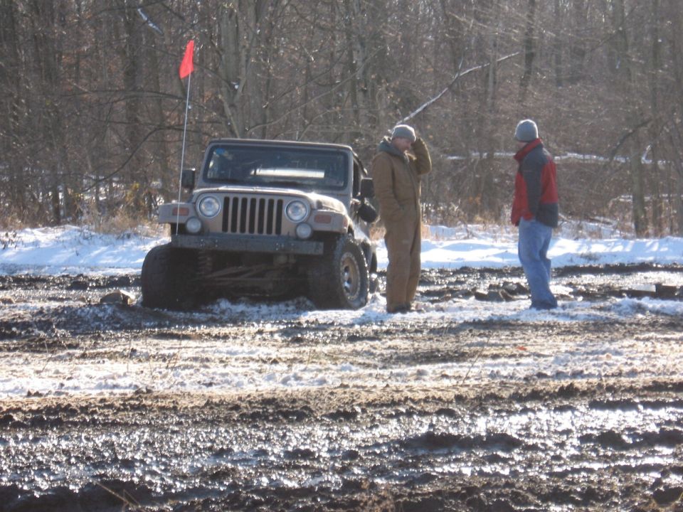 Jeep Wrangler stuck in mud, two men standing nearby in winter conditions. Red flag on antenna