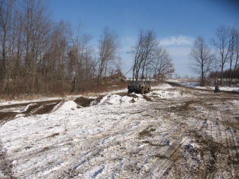 1979 Ford Bronco - An SUV drives through a snowy and muddy terrain under a clear blue sky.