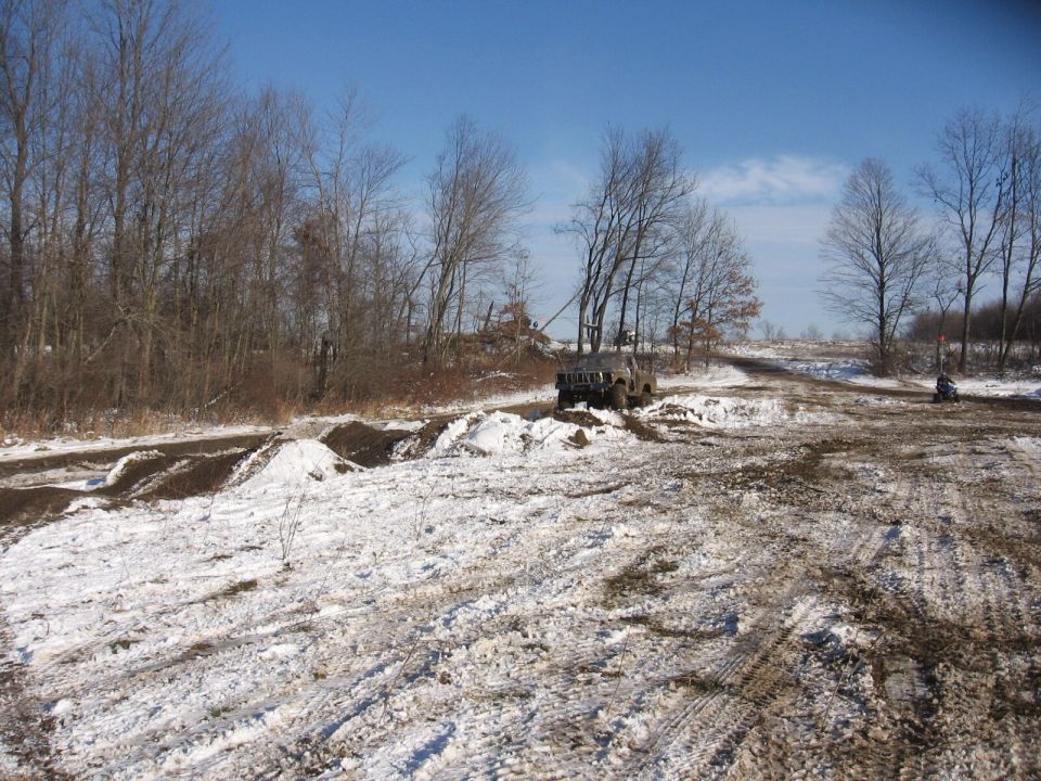 Dark SUV navigating a snowy and muddy off-road course with trees in the background