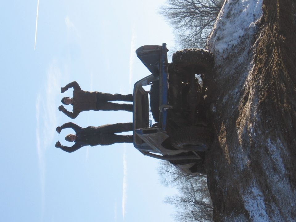 off-road vehicle tipped onto its side on a muddy bank with two people standing near it