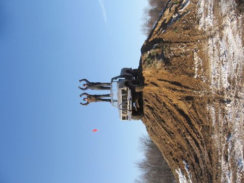 1979 Ford Bronco - Two individuals stand atop a muddy truck precariously balanced on a dirt hill, with a red flag visible in the distance.