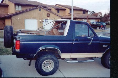 1990 Ford Bronco - The rear view of a dark blue 1990 Ford Bronco shows its spare tire and tan lower body trim.