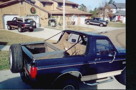 1990 Ford Bronco - Two Broncos and a pickup truck are parked in a suburban driveway during the holidays.