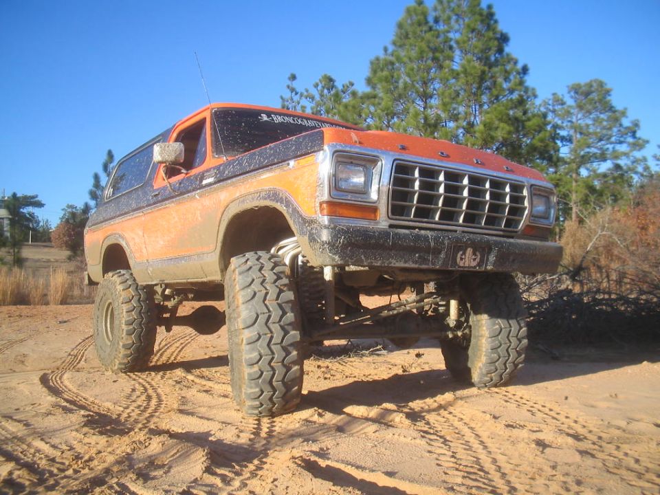 Lifted orange and black Ford Bronco on a dirt road. It has large off-road tires and a lifted suspension