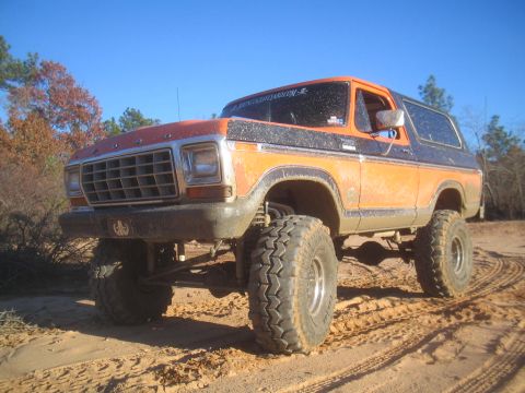 1979 Ford Bronco - This lifted 1978 Ford Bronco, painted orange and black, navigates sandy terrain with its large off-road tires.
