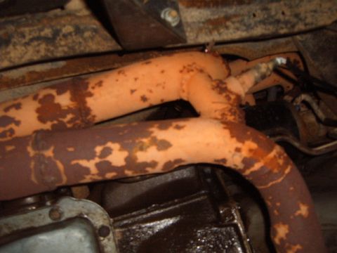 1988 Ford Bronco - Close-up view of heavily rusted exhaust pipes and part of the vehicle's transmission.