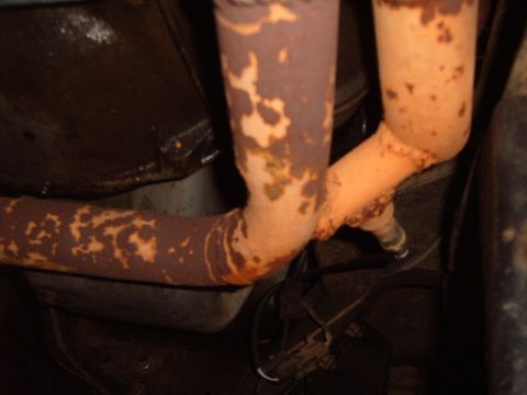 1988 Ford Bronco - Close-up view of heavily rusted exhaust pipes, showing a sensor attached to one of the pipes.