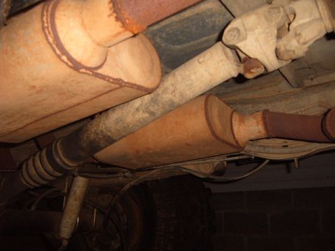 1988 Ford Bronco - The underside of a vehicle shows a heavily rusted exhaust system, including mufflers and a catalytic converter.