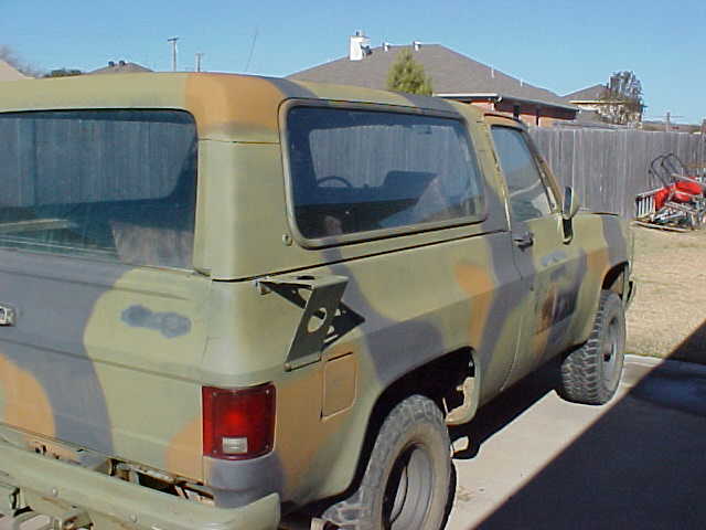 Camouflaged Chevrolet K5 Blazer, rear quarter view, showing damage on the tailgate