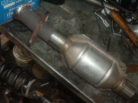1989 Ford Escort - Close-up of a catalytic converter, likely a replacement part, on a cluttered workbench.