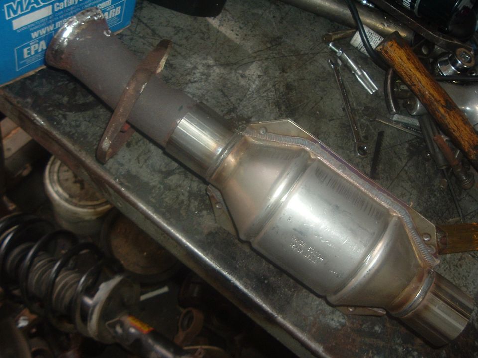 Catalytic converter with metal flanges on a workbench, tools and car parts in background