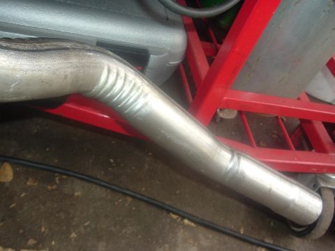 1989 Ford Escort - A section of a metal exhaust pipe is shown, with visible bends and seams, resting on a red rack.