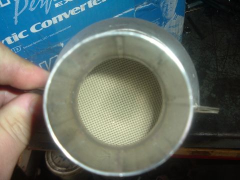 1989 Ford Escort - A close-up shows the internal ceramic honeycomb structure of a catalytic converter, with visible text on a box in the background.
