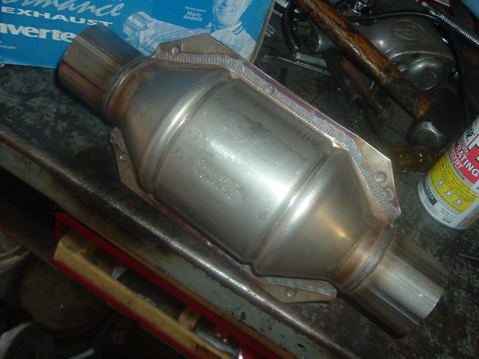 Catalytic converter with part number stamped on its side, resting on a workbench