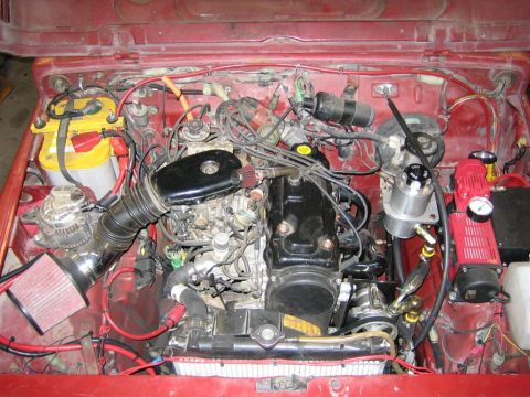 1987 Suzuki Samurai - The engine bay of a red vehicle shows a complex arrangement of mechanical components and wiring.