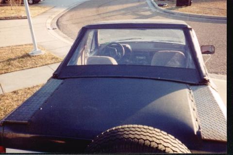 1990 Ford Bronco - Rear view of a dark blue convertible SUV, identified as a 1990 Ford Bronco, with a spare tire mounted externally.