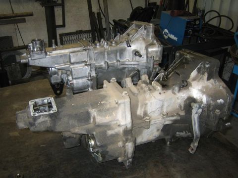 1987 Suzuki Samurai - Two vehicle transmissions sit on a workbench in a garage setting, with a welding machine visible in the background.