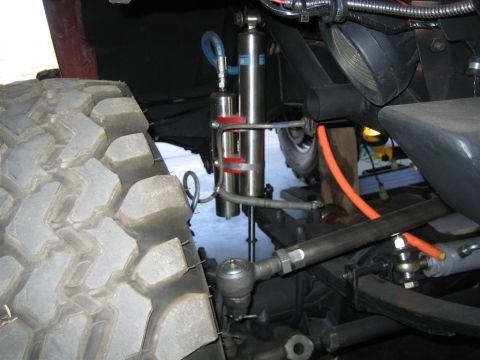 1987 Suzuki Samurai - Close-up view of off-road suspension components, including dual shock absorbers and a large, aggressive tire tread.