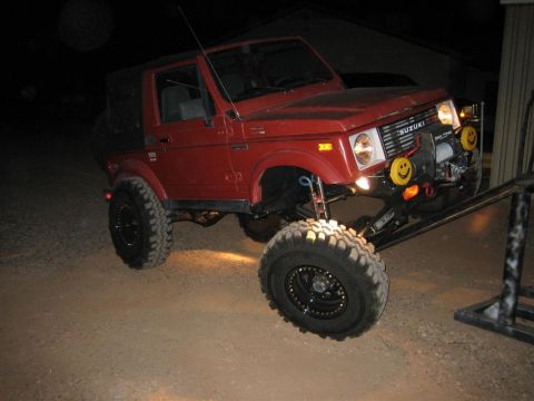 1987 Suzuki Samurai - Red 1987 Suzuki Samurai with off-road modifications, including a winch and large tires, positioned on a ramp.