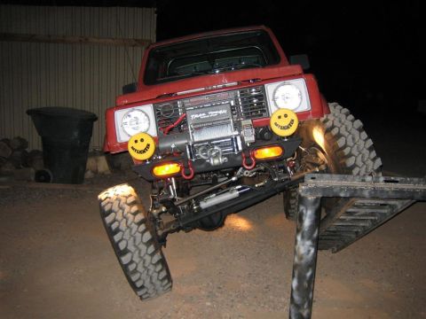 1987 Suzuki Samurai - A red 1987 Suzuki Samurai is shown with its front wheels on a platform, demonstrating its off-road capabilities.