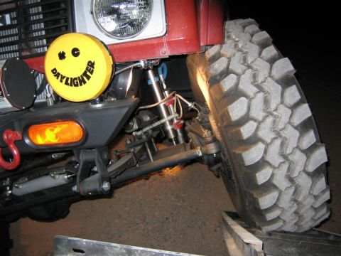 1987 Suzuki Samurai - Close-up of a red off-road vehicle's front wheel, suspension, and a yellow Daylighter lamp.