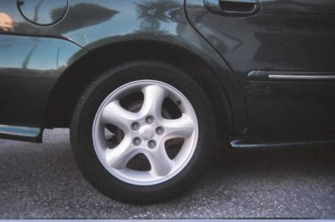 1999 Mercury Sable - A close-up view of the rear wheel and fender of a dark green sedan, revealing its body style and alloy wheel design.