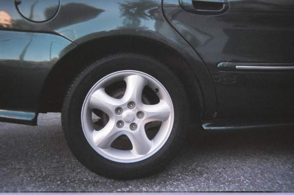 Five-spoke silver alloy wheel on a dark green sedan, close-up rear wheel view