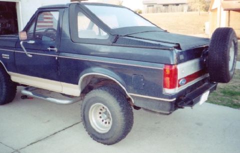1990 Ford Bronco - This dark blue SUV features a spare tire mounted on the rear, consistent with a 1990 Ford Bronco.