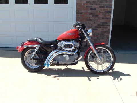 2002 Harley-Davidson Sportster Custom - A red Harley-Davidson motorcycle is parked in front of a garage door and brick wall.