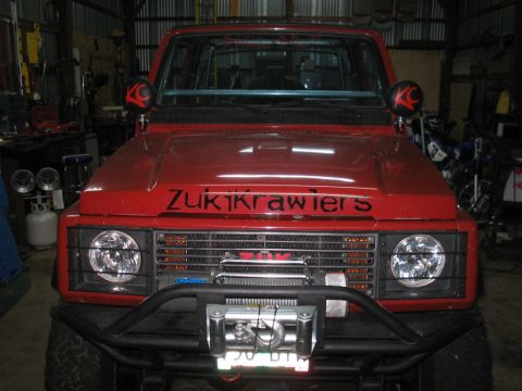 1987 Suzuki Samurai - A red 1987 Suzuki Samurai is parked inside a garage, equipped with a winch and custom decals.