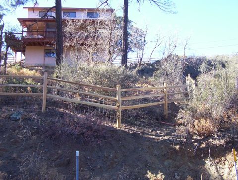 1995 Ford Bronco - A split rail fence with wire mesh separates a hillside from a house and trees.