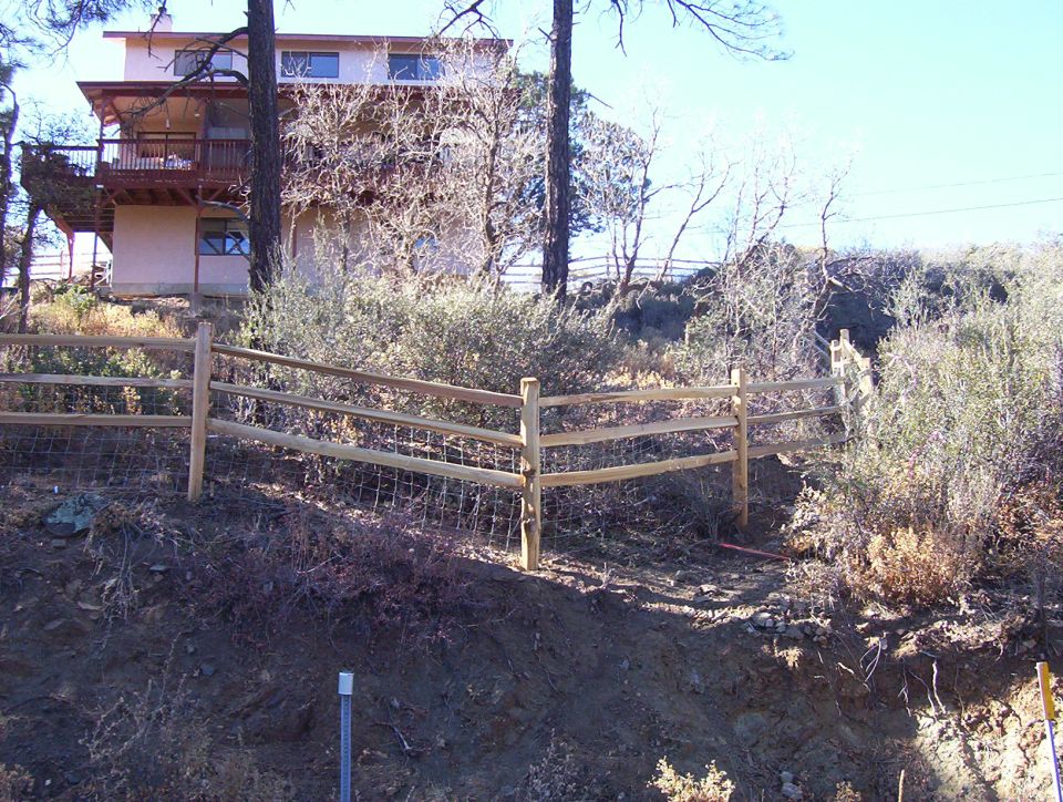 Split rail fence in front of a house on a wooded hillside