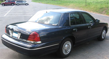 1999 Ford Crown Victoria - A dark blue sedan is parked in a lot, viewed from the rear quarter angle.