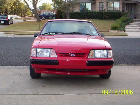 1990 Ford Mustang - A red 1990 Ford Mustang is parked in front of a house, with another vehicle in the background.
