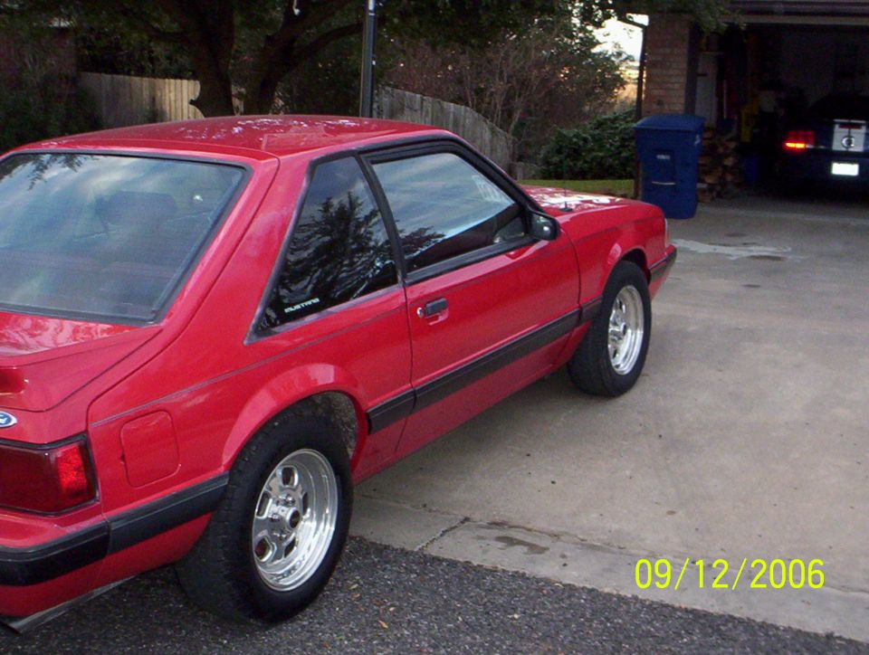 Red 1990 Ford Mustang parked in a driveway. Another car is visible in the garage behind it