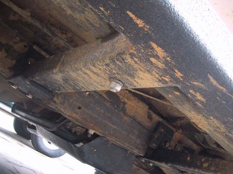 1995 Ford Bronco - The underside of a vehicle reveals its frame and suspension parts, covered in dirt and rust.