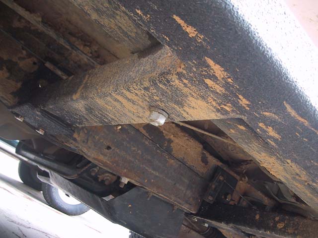 Underside view of a bedliner-coated slider mount gusset bolted to a rusty truck frame