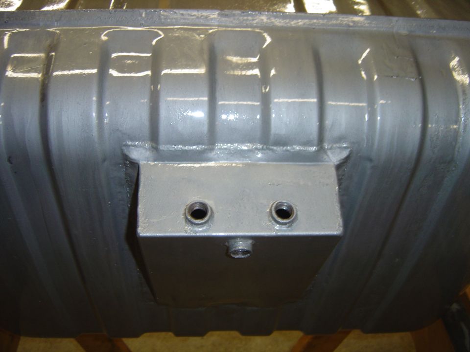 Close-up of a gray fuel tank with a metal bracket attached, showing two threaded fittings