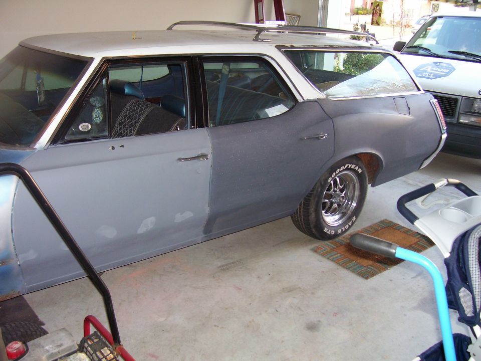 Gray-primered classic station wagon with white roof and chrome roof rack in a garage, side view