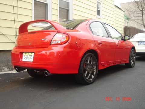 2005 Dodge SRT-4 - A red 2005 Dodge SRT-4 is parked outside a building, showing its distinctive rear spoiler and dual exhaust pipes.