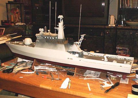 1998 Ford Crown Victoria - A model ship is shown on a table covered in crafting supplies, with a television and shelves in the background.
