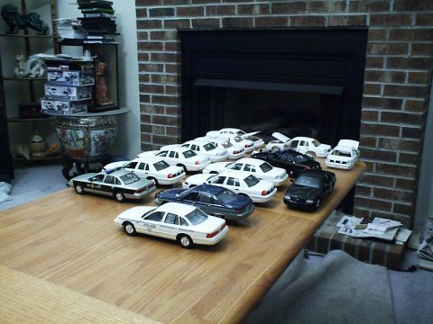 1998 Ford Crown Victoria - Many model cars are displayed on a table, with a brick fireplace in the background.