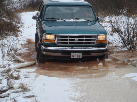 1996 Ford Bronco - A green SUV navigates a challenging path through mud and ice during winter conditions.